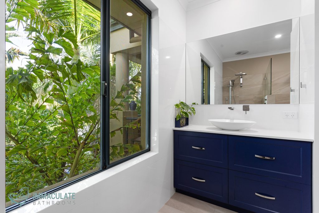 Modern Perth bathroom renovation with navy vanity, vessel basin and large window overlooking lush greenery – Immaculate Bathrooms Perth.