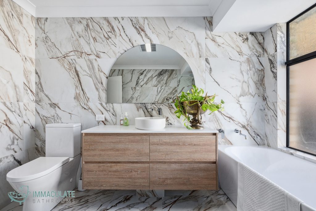 Modern bathroom renovation in Perth featuring marble-look tiles, floating timber vanity and freestanding bathtub.