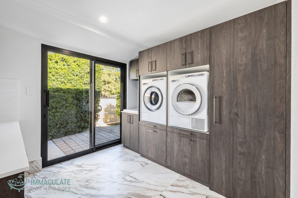 Modern laundry renovation with built-in washer and dryer, dark wood cabinetry and large sliding glass door.