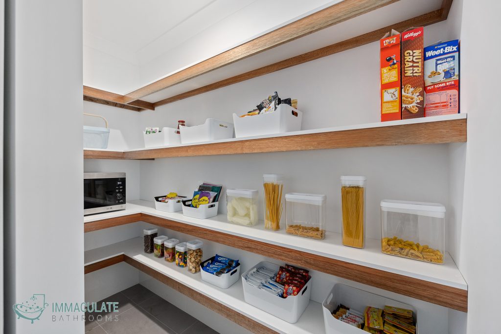 Organised modern walk-in pantry with timber floating shelves, white storage containers, labelled food jars and a built-in microwave.