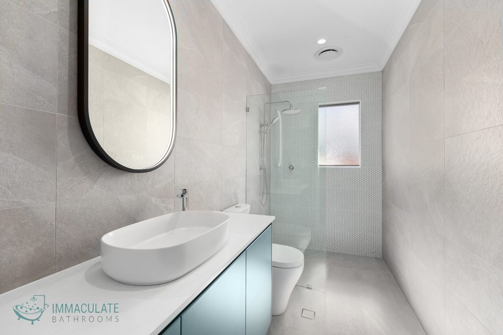 Modern bathroom renovation with light grey large-format tiles, walk-in shower, oval vessel sink, and frameless glass screen.