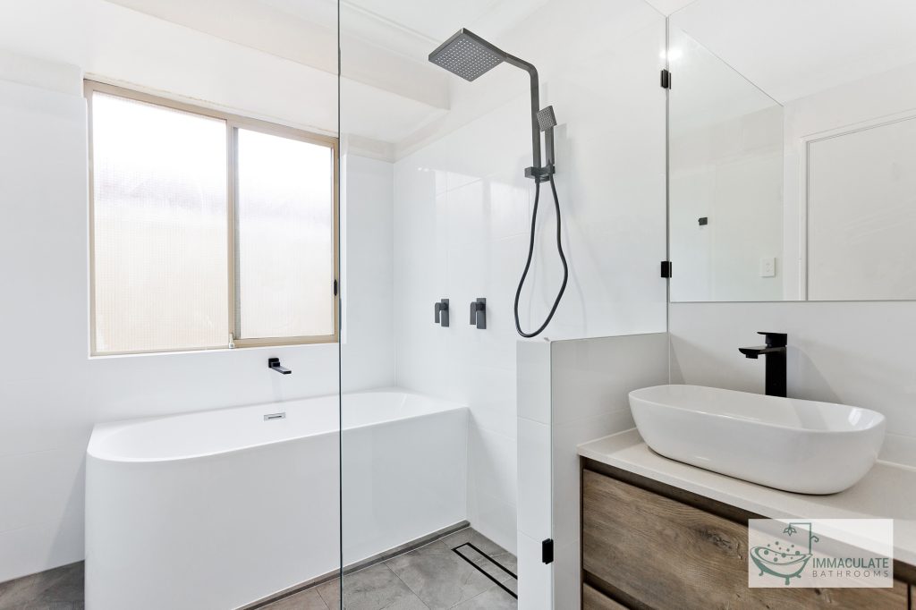 Modern bathroom renovation featuring a freestanding bathtub, frameless glass shower, square rainfall showerhead, black fixtures, and a timber floating vanity.