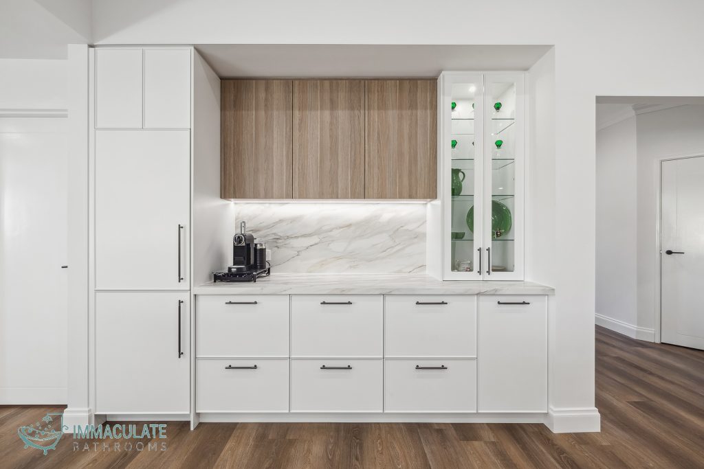Modern white kitchen cabinetry with marble-look splashback, wooden overhead cupboards, glass display cabinet and coffee station.