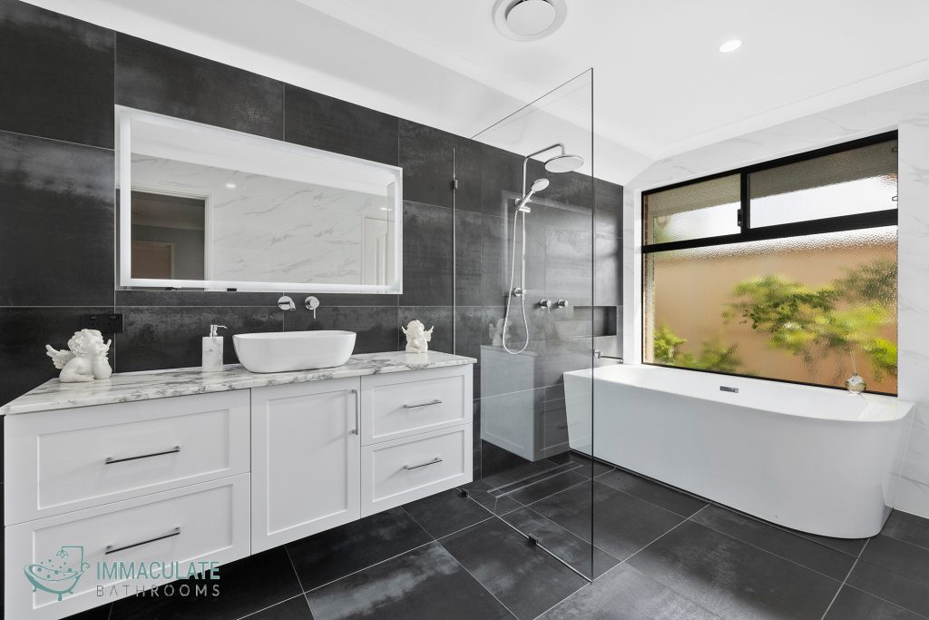 Modern bathroom renovation with white vanity, stone benchtop, black feature tiles, walk-in shower, and freestanding bathtub.