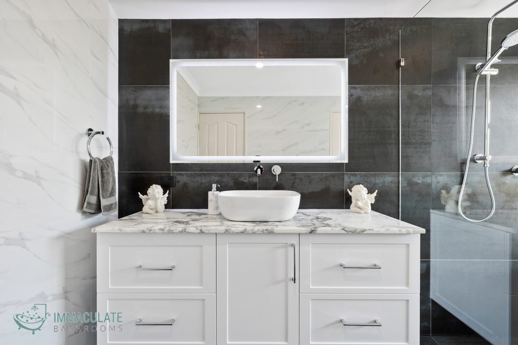 Modern bathroom renovation with white marble vanity, vessel sink, LED-lit mirror and dark feature tiles by Immaculate Bathrooms Perth.