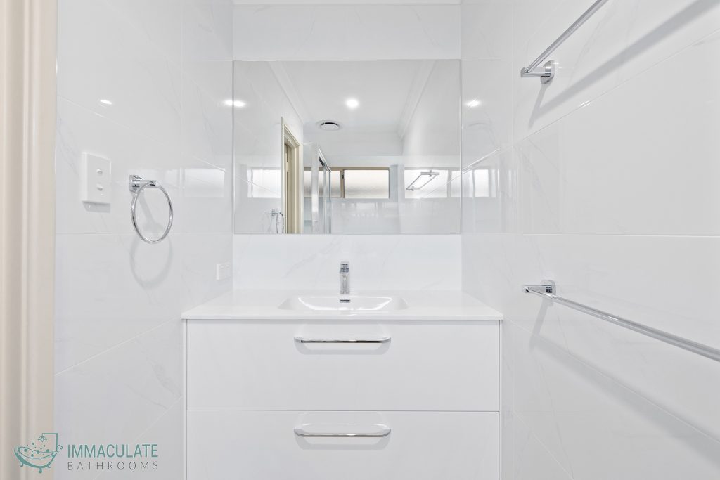 Modern white bathroom vanity with large mirror, chrome tapware and marble-look wall tiles — Immaculate Bathrooms Perth renovation.