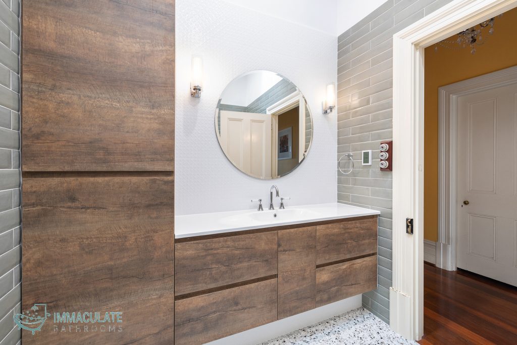 Modern bathroom with timber-look vanity, round mirror, terrazzo flooring and glossy grey subway tiles – Immaculate Bathrooms Perth