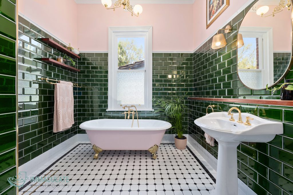 Victorian-style bathroom with dark green subway tiles, a pink clawfoot bathtub with gold fittings, pedestal basin and heritage lighting.