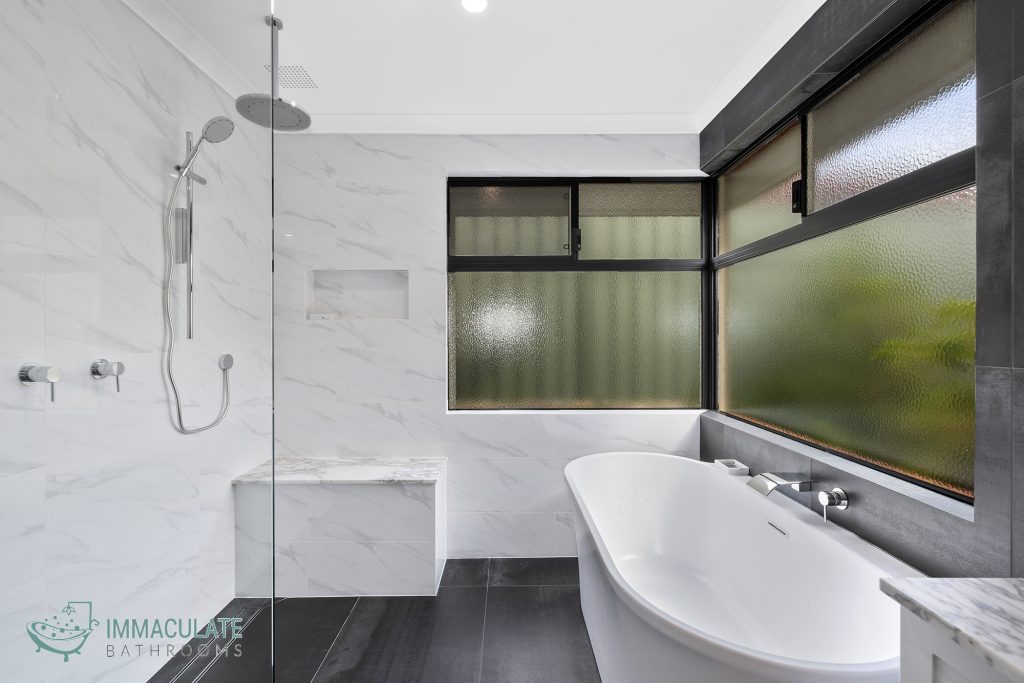 Modern bathroom renovation with freestanding bathtub, large frosted windows, marble-look tiles and walk-in shower.