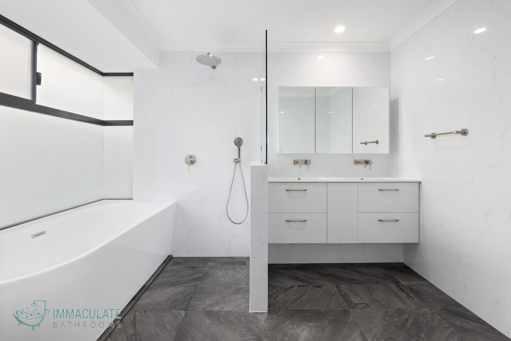 Modern white bathroom renovation featuring a freestanding bath, walk-in shower with matte nickel fixtures, double vanity with mirrored cabinets, and large frosted windows by Immaculate Bathrooms Perth.