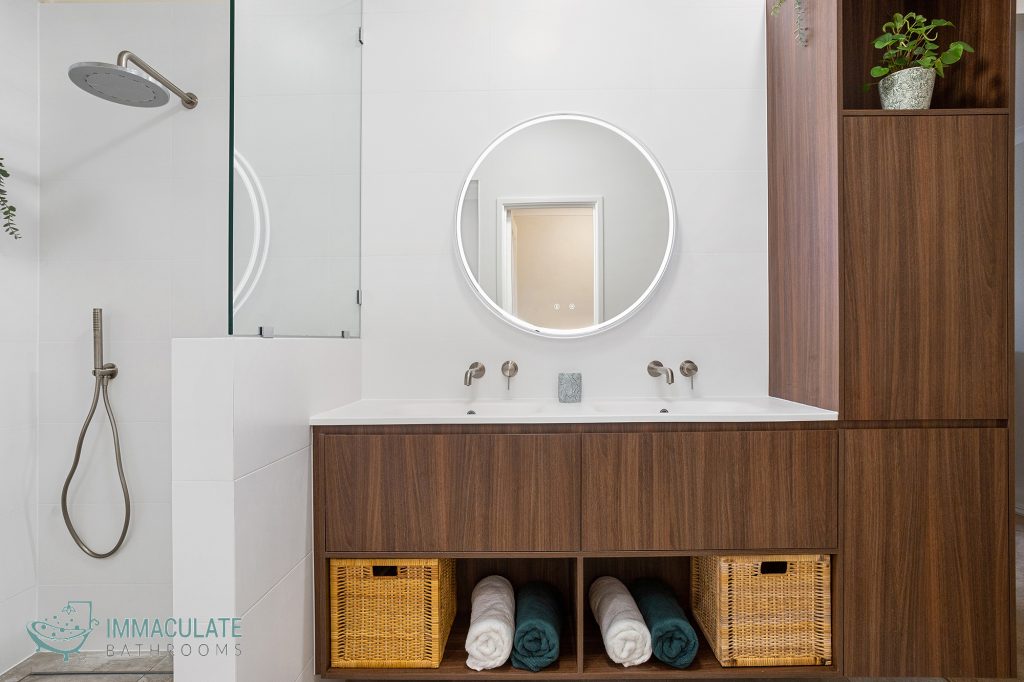 Modern bathroom featuring a circular LED mirror, double vanity with walnut cabinetry, built-in bathtub, and walk-in shower with brushed nickel fixtures.