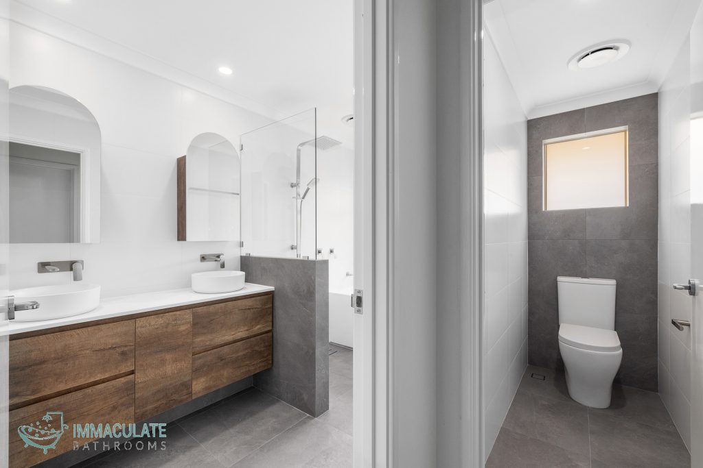 Modern Perth bathroom renovation featuring double vanity with timber cabinetry, walk-in shower and separate toilet with grey floor-to-ceiling tiles.