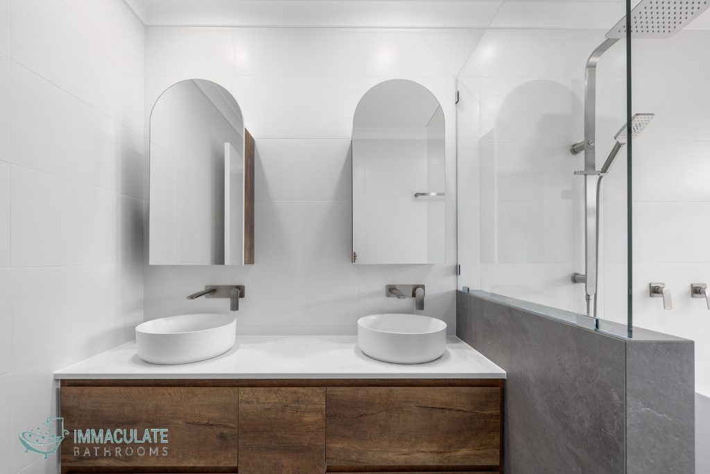 Modern ensuite bathroom renovation with twin vessel sinks, timber vanity, arched mirrored cabinets, and walk-in shower with brushed nickel fixtures.