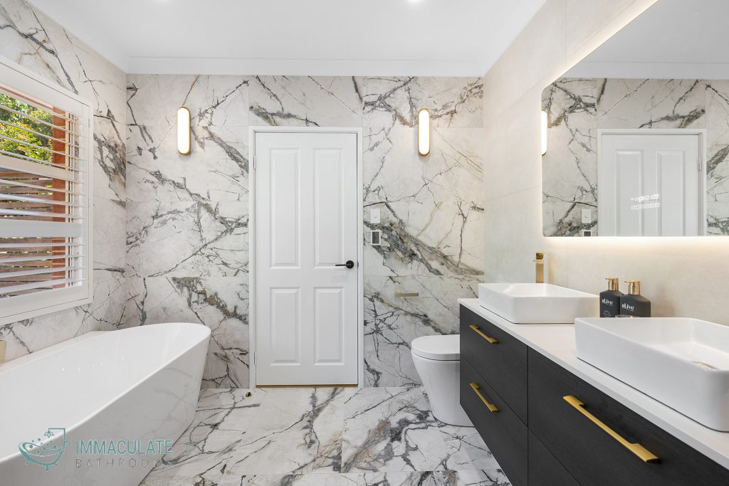 Modern luxury bathroom in Perth featuring freestanding bath, dual vanity with black cabinetry and gold handles, and marble-style tiles – Immaculate Bathrooms renovation.