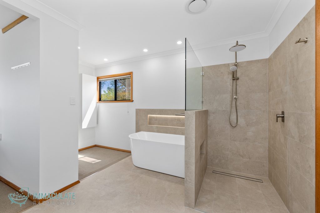 Modern bathroom renovation featuring a freestanding bathtub, walk-in shower, large beige tiles, niche lighting, and minimalist fixtures — Immaculate Bathrooms Perth.
