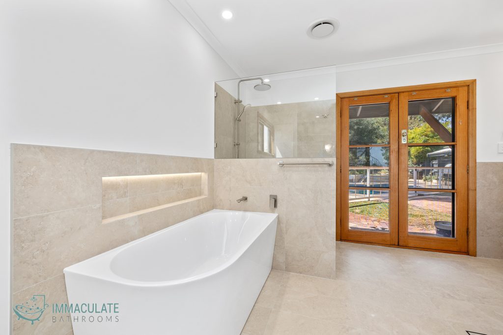 Modern bathroom with freestanding bath, beige tiles, built-in LED niche and glass shower screen by Immaculate Bathrooms Perth