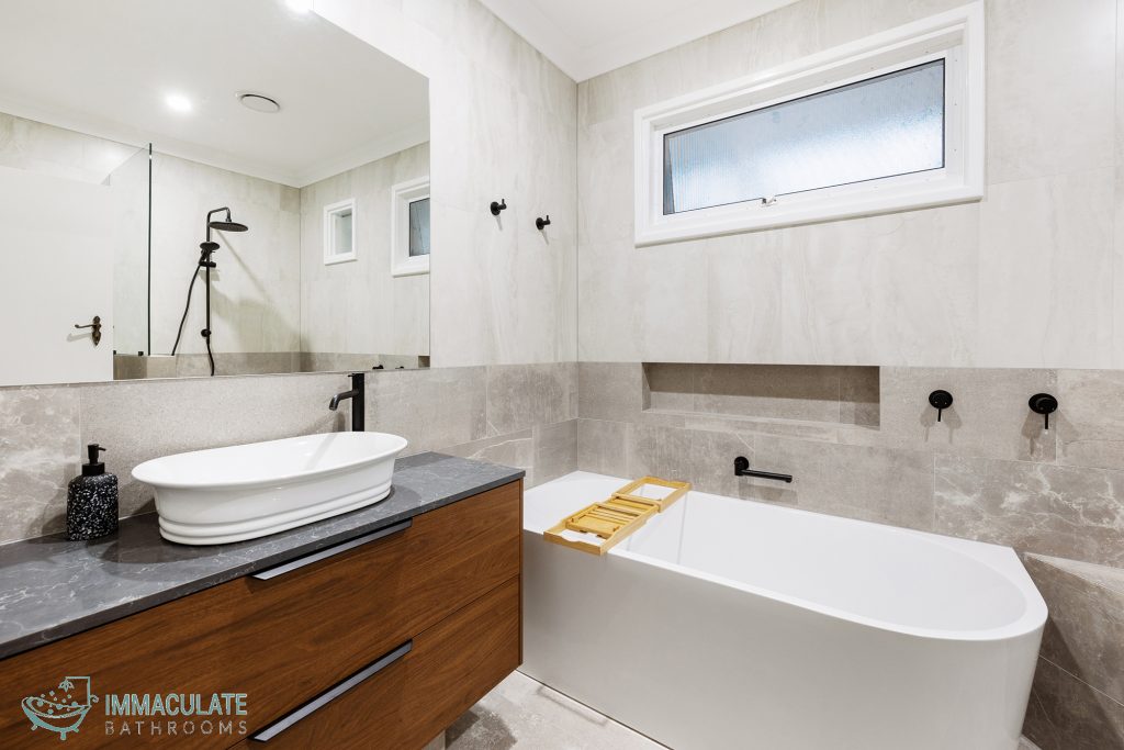 Modern bathroom with timber vanity, freestanding bath, matte black tapware and stone-look tiles by Immaculate Bathrooms Perth