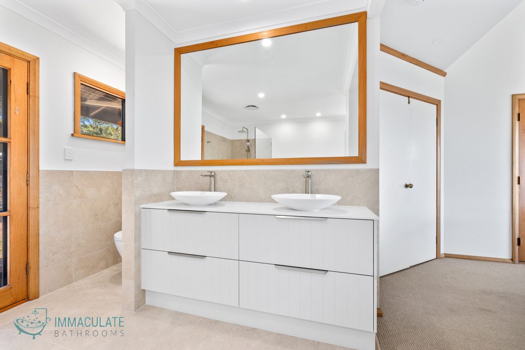 Bright ensuite bathroom with double white vanity, vessel basins, large timber-framed mirror and beige floor tiles by Immaculate Bathrooms Perth