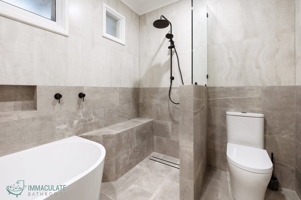 Modern bathroom with stone-look tiles, built-in shower bench, freestanding bath and matte black tapware by Immaculate Bathrooms Perth