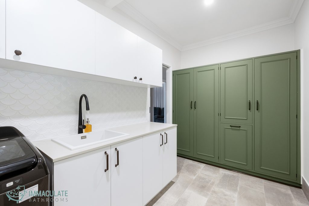 Modern laundry with white cabinetry, black tapware, textured white splashback and green storage cupboards by Immaculate Bathrooms Perth