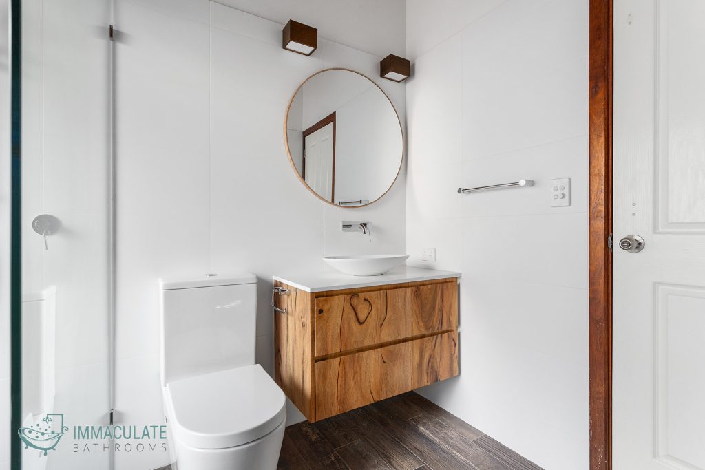 Small modern bathroom with timber floating vanity, round mirror, vessel basin and white tiled walls by Immaculate Bathrooms Perth
