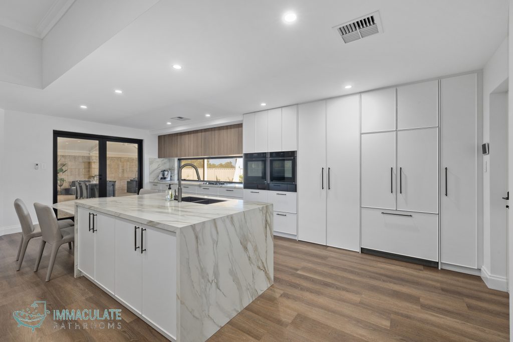 Modern kitchen renovation in Perth with marble island benchtop, white cabinetry, and timber flooring by Immaculate Bathrooms Perth.