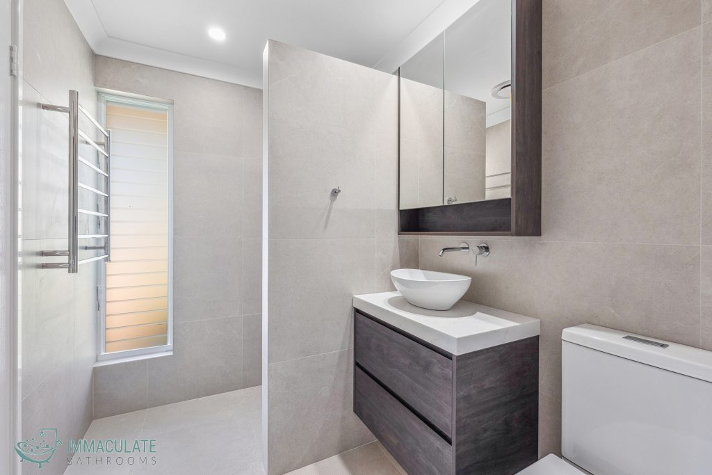 Modern bathroom renovation featuring a walk-in shower, large vanity with vessel sink, mirrored cabinet, and neutral stone-look tiles.