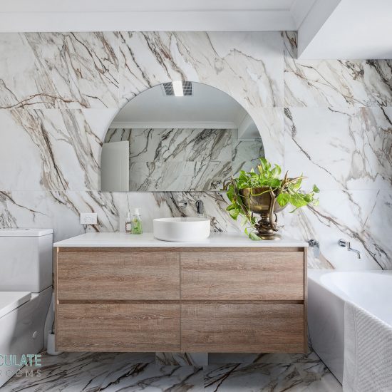 Luxury bathroom renovation in Perth with marble feature walls, floating timber vanity, round mirror, and freestanding bath by Immaculate Bathrooms.